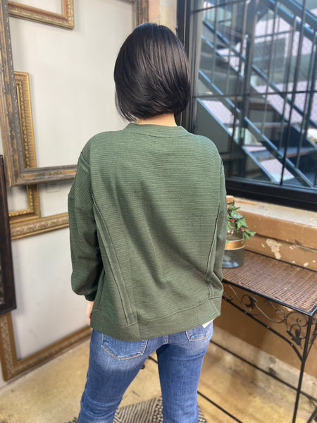 Back view of a hunter green v neck long sleeve top from Blu Pepper with exposed seams and side slits