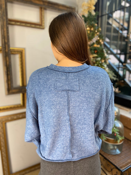 Back view of a blue colored brushed hacci knit top with long sleeves and exposed seams.