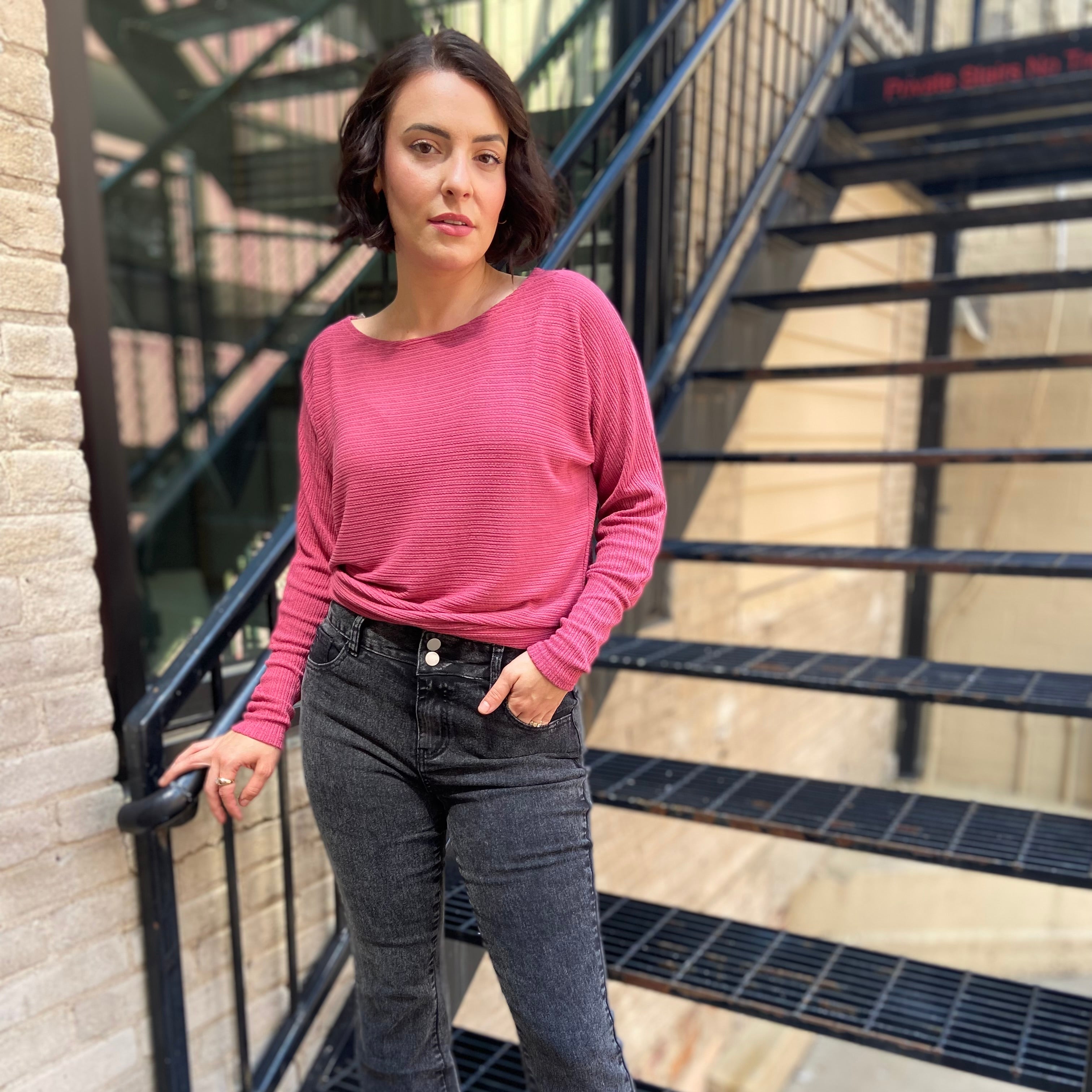 Woman in a pink sweater and dark jeans standing on a staircase.