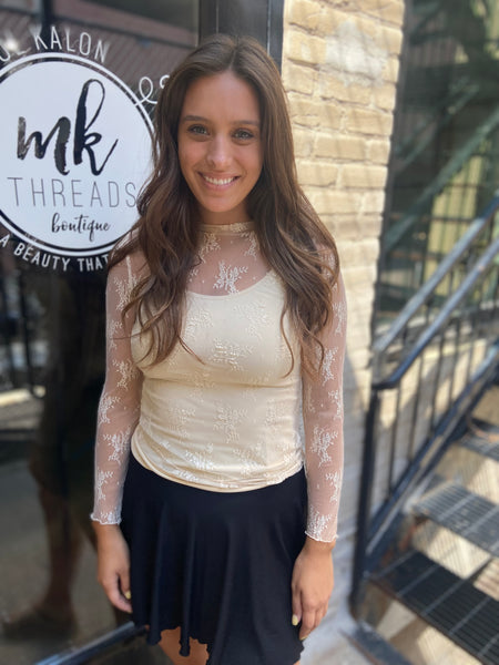 Beige colored sheer lace long sleeve top paired over a beige cami with a black mini skirt