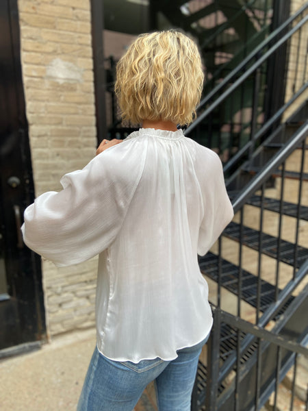 Back view of an ivory satin blouse paired with blue jeans