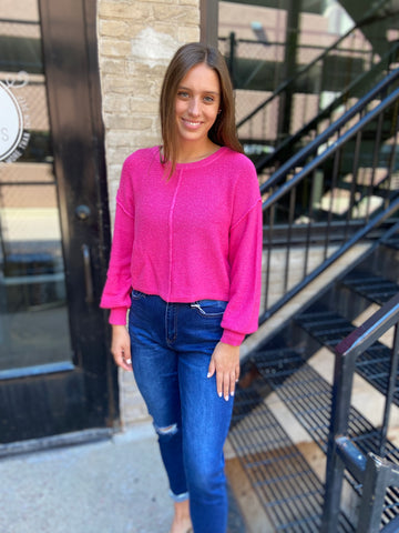 Fuchsia textured sweater cropped to the waist paired with blue jeans