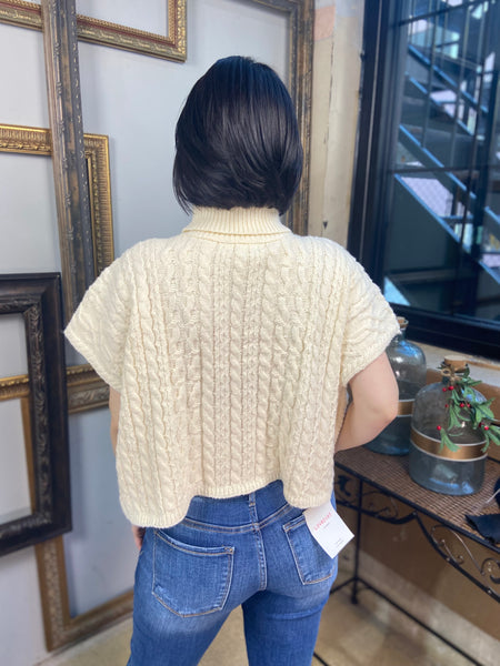 Back view of a cream colored short sleeved cable knit sweater with turtle neck from Blu Pepper