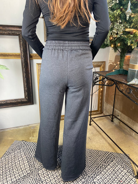 Back view of a pair of Charcoal colored fleece drawstring sweatpants with pockets and wide legs