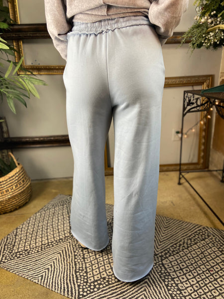 Back view of a pair of light blue fleece lined drawstring sweatpants with pockets and wide legs