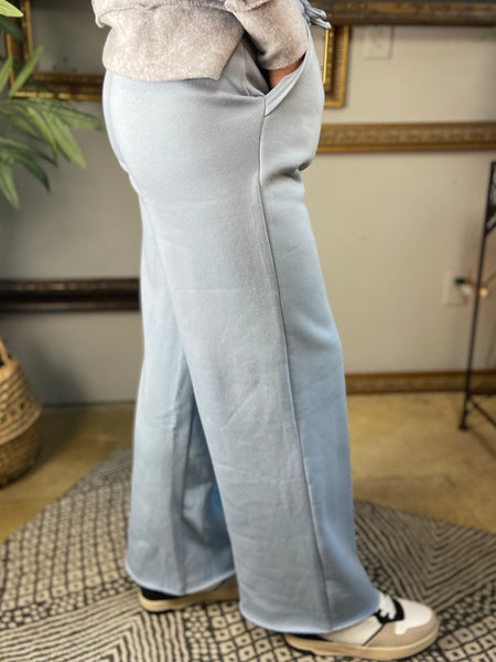 Side view of a Pair of light blue fleece lined drawstring sweatpants with pockets and wide legs