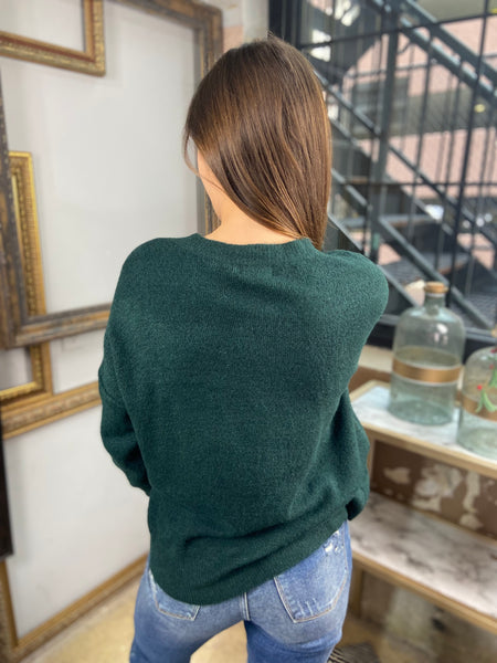 Back view of a deep green colored sweater paired with blue jeans