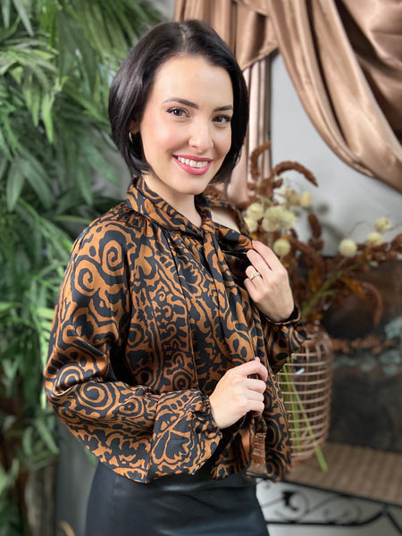 Side view of a brown and black abstract print long sleeved blouse with neck tie and shoulder cut out