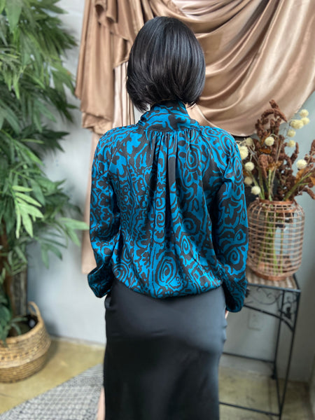 Back view of a teal and black abstract print blouse paired with a black satin midi skirt