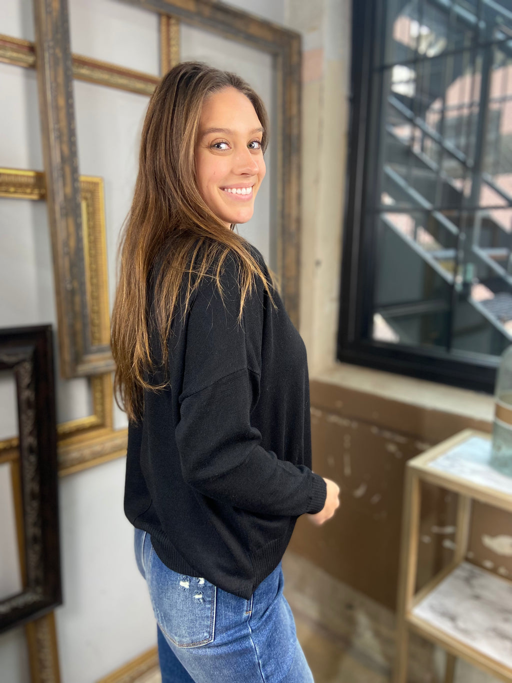 Side view of a black sweater from Blu Pepper with drop shoulders paired with blue jeans