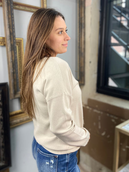 Side view of a light taupe colored sweater with drop shoulders paired with blue jeans