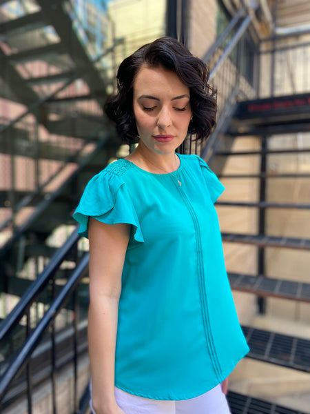 Introducing the Kezia Light Teal Ruffle Sleeve Blouse, your new go-to for effortless elegance. This blouse effortlessly combines classic style with a modern twist, featuring:

- Delicate lace trim for a feminine flair
- Flattering tulip sleeves that add grace to any outfit
- Chic pintuck detailing on the front for a refined look
- Keyhole button closure at the back that enhances its charm